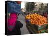 Palestinian Woman in Colourful Scarf and Carrying Bag on Her Head Walking Past an Orange Stall-Eitan Simanor-Stretched Canvas