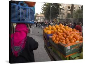 Palestinian Woman in Colourful Scarf and Carrying Bag on Her Head Walking Past an Orange Stall-Eitan Simanor-Stretched Canvas