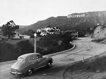 1950s AUSTIN CAR DRIVING UP THE HOLLYWOOD HILLS WITH HOLLYWOOD SIGN IN DISTANCE LOS ANGELES CA USA-Panoramic Images-Photographic Print