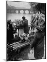 Parisian Flower Vendor at Work Stocking His Stall on the Seine with the Pont Neuf in the Background-Ed Clark-Mounted Photographic Print