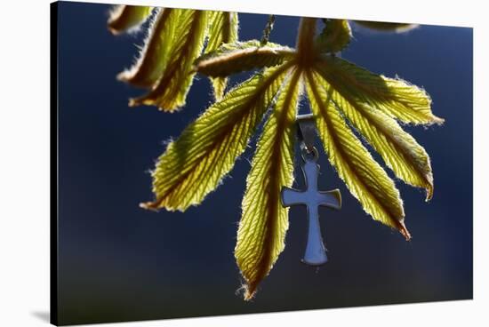 Pendant with cross on a young green chestnut leaf at springtime-null-Stretched Canvas