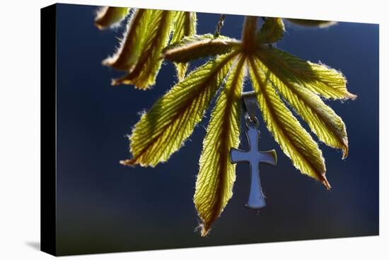 Pendant with cross on a young green chestnut leaf at springtime-null-Stretched Canvas