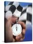 Person's Hand Holding a Stopwatch in Front of a Checkered Flag-null-Stretched Canvas