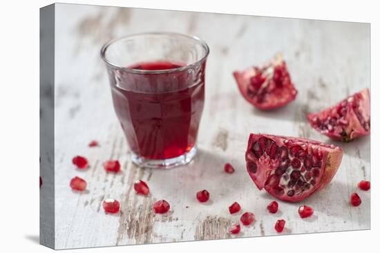 Pomegranate Pieces and a Glass of Pomegranate Juice on White Wooden Table-Jana Ihle-Stretched Canvas