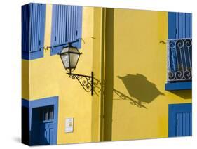 Portugal, Aveiro. Shadow of street lantern on colorful yellow building with bright blue shutters.-Julie Eggers-Stretched Canvas