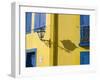 Portugal, Aveiro. Shadow of street lantern on colorful yellow building with bright blue shutters.-Julie Eggers-Framed Photographic Print