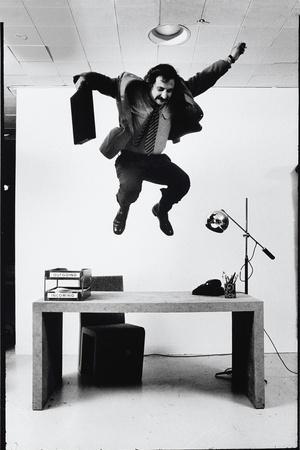 Architect and Designer Frank Gehry Jumping on a Desk in His Line of Cardboard Furniture