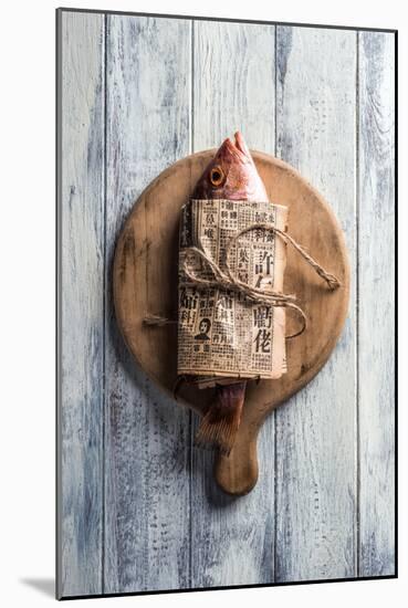 Red Snapper Wrapped in Chinese Newspaper on Wooden Background-Gary Jones-Mounted Photographic Print