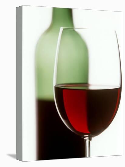 Red Wine Glass with Half-Full Wine Bottle in Background-Joerg Lehmann-Stretched Canvas