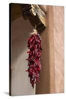 Santa Fe, New Mexico. Long, red chili, hanging from a wooden corbel and stucco wall-Jolly Sienda-Stretched Canvas