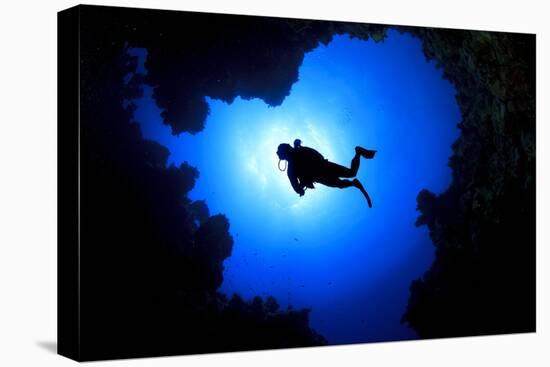 Scuba Diver Swims over Underwater Cave, Silhouette against Sun-Rich Carey-Stretched Canvas