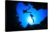 Scuba Divers Descend into an Underwater Cavern. Silhouettes against Sunburst-Rich Carey-Stretched Canvas