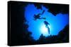 Scuba Divers Descend into an Underwater Cavern. Silhouettes against Sunburst-Rich Carey-Stretched Canvas