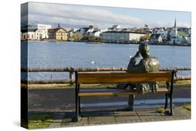 Sculpture of a man sitting on a park bench in front of Tjornin Lake and the Historic Centre of Rykj-Miles Ertman-Stretched Canvas