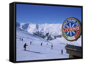 Sign with Skiers and Mountains in the Background at the Ski Resort of Livigno in Northern Italy-Teegan Tom-Framed Stretched Canvas