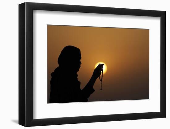 Silhouette of a Muslim woman holding prayer beads in her hands and praying at sunset-Godong-Framed Photographic Print