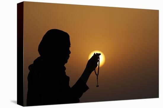 Silhouette of a Muslim woman holding prayer beads in her hands and praying at sunset-Godong-Stretched Canvas