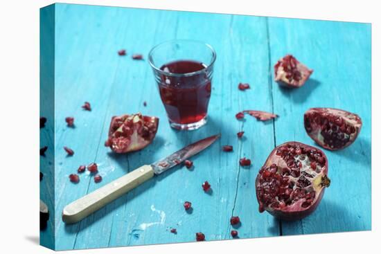 Sliced Pomegranate and a Glass of Pomegranate Juice on Turquoise Wooden Table-Jana Ihle-Stretched Canvas