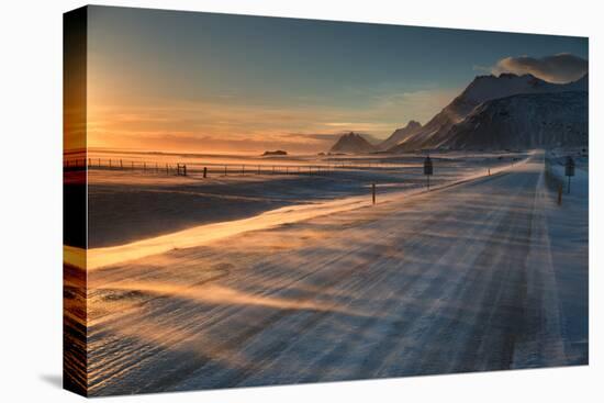 Snow Blows across an Icelandic Road at Sunrise with Mountains Looming in the Distance-Alex Saberi-Stretched Canvas