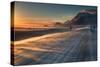 Snow Blows across an Icelandic Road at Sunrise with Mountains Looming in the Distance-Alex Saberi-Stretched Canvas