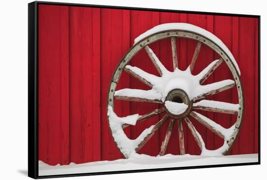 Snow-covered wagon wheels against red barn near town of Banff, Canadian Rockies, Alberta, Canada-Stuart Westmorland-Framed Stretched Canvas