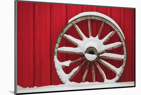 Snow-covered wagon wheels against red barn near town of Banff, Canadian Rockies, Alberta, Canada-Stuart Westmorland-Mounted Photographic Print