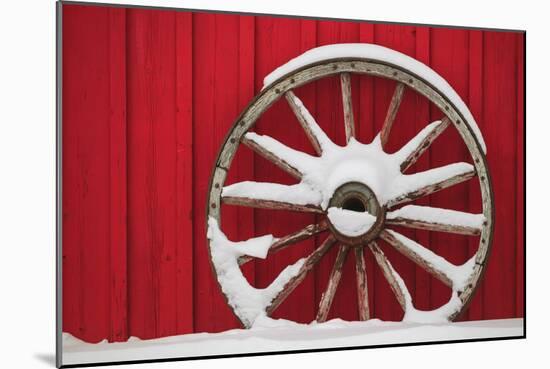 Snow-covered wagon wheels against red barn near town of Banff, Canadian Rockies, Alberta, Canada-Stuart Westmorland-Mounted Photographic Print