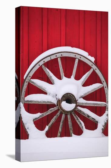 Snow-covered wagon wheels against red barn near town of Banff, Canadian Rockies, Alberta, Canada-Stuart Westmorland-Stretched Canvas
