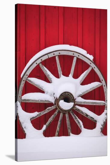 Snow-covered wagon wheels against red barn near town of Banff, Canadian Rockies, Alberta, Canada-Stuart Westmorland-Stretched Canvas