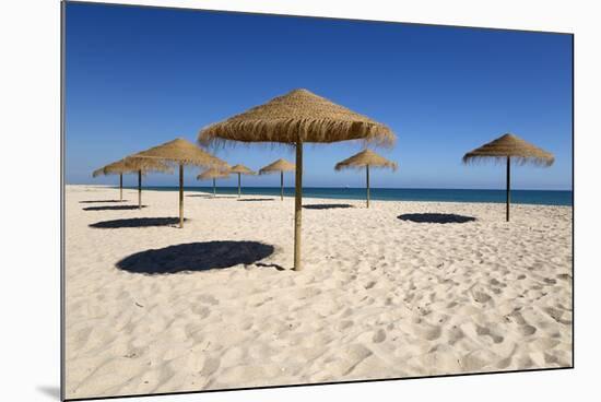 Straw umbrellas on empty white sand beach with clear sea behind, Ilha do Farol, Culatra Barrier Isl-Stuart Black-Mounted Photographic Print