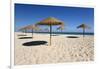 Straw umbrellas on empty white sand beach with clear sea behind, Ilha do Farol, Culatra Barrier Isl-Stuart Black-Framed Photographic Print