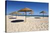 Straw umbrellas on empty white sand beach with clear sea behind, Ilha do Farol, Culatra Barrier Isl-Stuart Black-Stretched Canvas