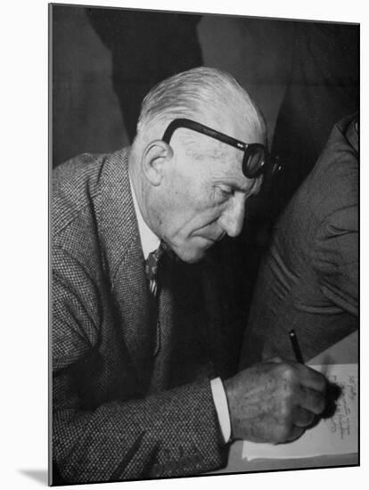 Swiss Architect Le Corbusier Leaning Down to Write with His Glasses Pushed Back on His Forehead-null-Mounted Photographic Print