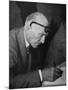 Swiss Architect Le Corbusier Leaning Down to Write with His Glasses Pushed Back on His Forehead-null-Mounted Photographic Print