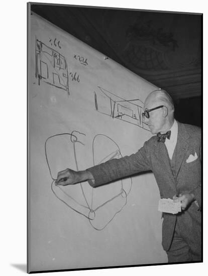 Swiss Architect Le Corbusier Standing on Stage with Notes in His Hand and Drawing on Sketch Pad-null-Mounted Photographic Print
