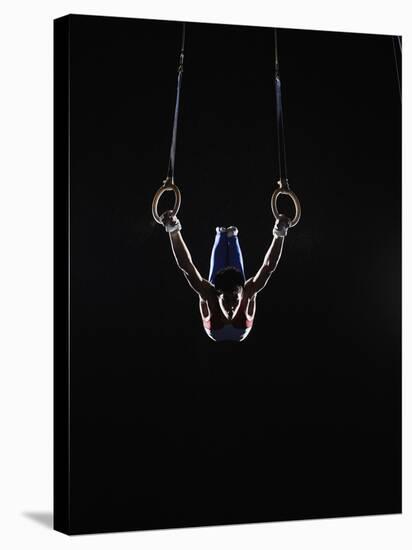 Teenage (16-17) Male Gymnast Practicing on Rings against Black Background-Thomas Barwick-Stretched Canvas