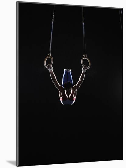 Teenage (16-17) Male Gymnast Practicing on Rings against Black Background-Thomas Barwick-Mounted Photographic Print