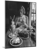 Teenaged Girl Sitting in Drugstore Eating a Hamburger-Hank Walker-Mounted Photographic Print