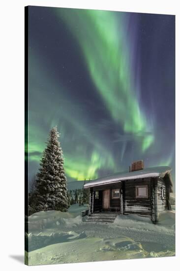 The Northern Lights (Aurora borealis) frame the wooden hut in the snowy woods, Pallas, Yllastunturi-Roberto Moiola-Stretched Canvas