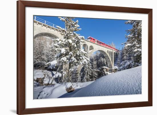 The red train on viaduct surrounded by snowy woods, Cinuos-Chel, Canton of Graubunden, Engadine, Sw-Roberto Moiola-Framed Photographic Print
