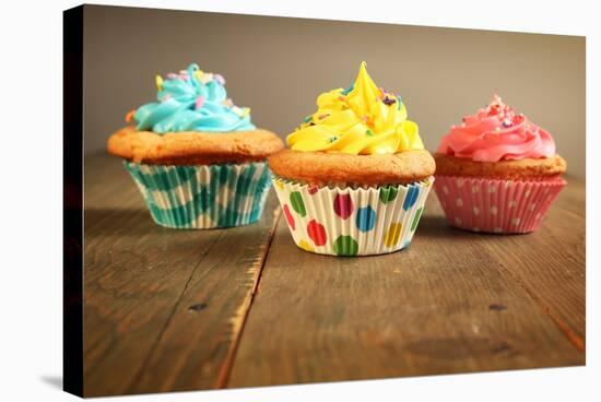 Three Different Colors Cupcakes On A Wooden Table, Blue, Yellow And Pink-pink candy-Stretched Canvas