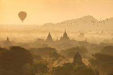 A hot air balloon flies over a trees and a temple at sunrise on a misty morning, Bagan, Myanmar-Tim Mannakee-Photographic Print