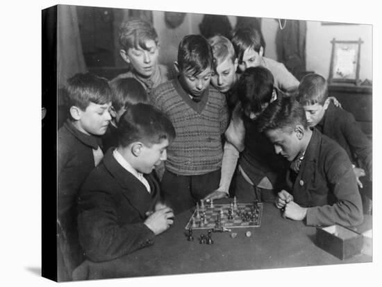 Two Boys Sit for a Game of Chess. Eight Spectators Look On-null-Stretched Canvas