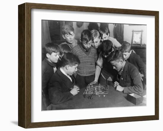 Two Boys Sit for a Game of Chess. Eight Spectators Look On-null-Framed Photographic Print