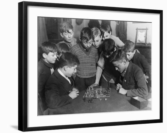 Two Boys Sit for a Game of Chess. Eight Spectators Look On-null-Framed Photographic Print