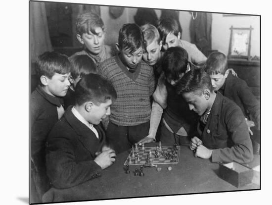 Two Boys Sit for a Game of Chess. Eight Spectators Look On-null-Mounted Photographic Print