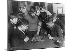 Two Boys Sit for a Game of Chess. Eight Spectators Look On-null-Mounted Photographic Print