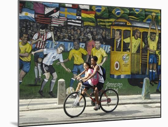 Two Children Ride Their Bicycle Pass a Mural-null-Mounted Photographic Print