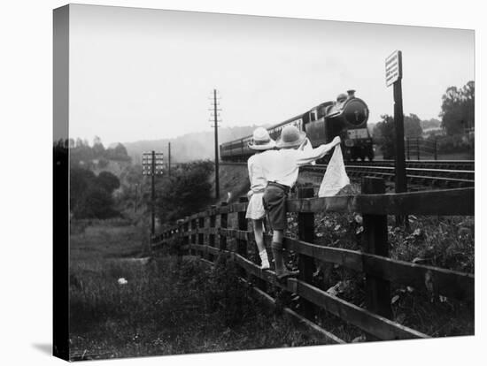 Two Children Stand on a Fence and Wave a Handkerchief at a Passing Steam Train-Staniland Pugh-Stretched Canvas