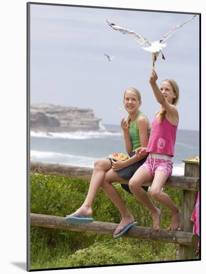 Two Girls Feeding Chips to a Seagull at the Beach-Louise Hammond-Mounted Photographic Print